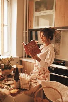 a woman standing in a kitchen reading a book