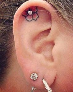 an ear tattoo with flowers on it and two piercings attached to the back of the ear