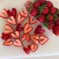 strawberries are arranged on a cutting board next to a container of sliced strawberries