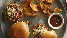 two pulled pork sliders with coleslaw and potato chips on a gray plate