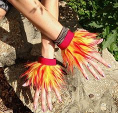 a woman's hand with red and yellow feathers on her fingers sitting on a rock