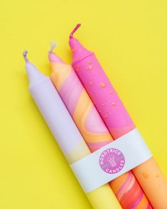 three different colored pens sitting next to each other on a yellow surface with water droplets