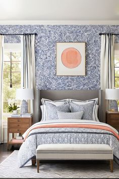 a bedroom with blue and white wallpaper, a bed, two lamps and a painting on the wall