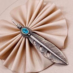 a brooch with a feather on it sitting on top of a cloth covered table