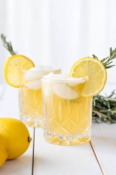 two glasses filled with lemonade sitting on top of a table next to lemons