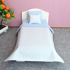 a bed with blue sheets and pillows next to a potted plant on the floor