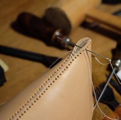 a close up of a sewing needle on a piece of leather with other tools in the background