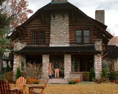 two people standing in front of a rustic log cabin with lawn chairs and fire pit