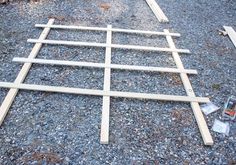 a wooden bed frame laying on top of gravel next to a pile of wood planks