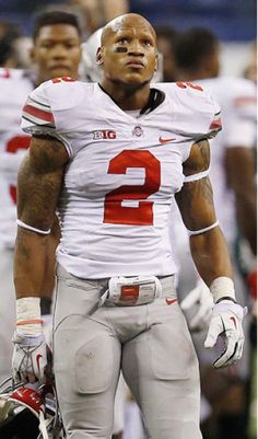 a close up of a football player holding a helmet on the field with other players in the background