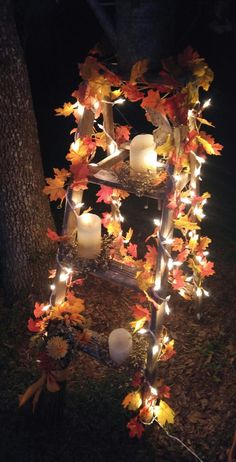 an old ladder decorated with fall leaves and lit candles in the middle of a yard