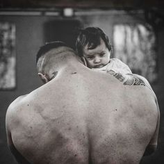 a man holding a baby in his arms and looking down at the ground with no shirt on