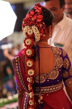 a woman wearing a red and blue sari with flowers in her hair is looking down