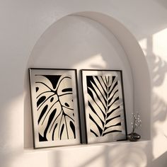 two black and white paintings on a wall next to a vase with flowers in it