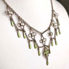 This antique silver and green and white enamel necklace was hand crated in the Arts and Crafts era, around 1910 by famed Norwegian silver smith Marius Hammer. Hammer lived from 1847-1927 and worked in Bergen, Norway. This drop necklace features flowers and drops of bright spring green and matte what enamel with that velvety look that Hammer was a master of. Chains of silver weave throughout this necklace, piecing together a lovely statement piece of swirls, loops, and twists. This piece weighs 10.3 grams and measures 16 inches in length. It has been acid tested. A mark on the back reads, ‘930S’, indicating fine silver and it bears the hallmark of the M with a hammer forming the center.  Wearable on a Saturday night date, give-able for a wedding present, presentable at a cocktail party, and Michael Michaud Necklace, Art Deco Hallmarked Enamel Jewelry, Formal Green Enamel Jewelry, Antique Enamel Necklace Hallmarked, Antique Enamel Necklace With Hallmark, Antique Enamel Hallmarked Necklaces, Antique Enamel Pendant Jewelry, Vintage Charm Round Enamel Jewelry, Round Enamel Jewelry With Vintage Charm