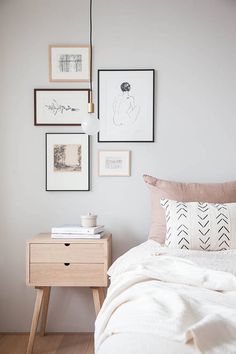 a white bed sitting next to a wooden table with pictures on the wall above it