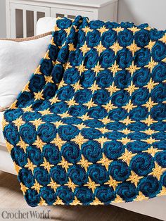 a crocheted blue and yellow blanket with gold stars on it sitting on a bed