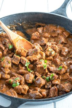 a skillet filled with meat and gravy on top of a wooden spoon