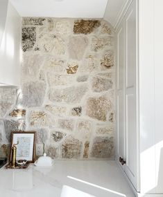 a stone wall in a kitchen with white cabinets and marble counter tops, along with a framed photograph