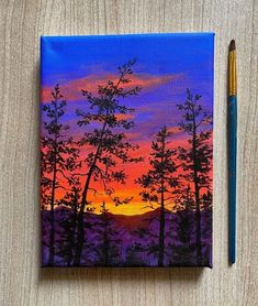 a painting of trees with the sun setting in the background and a pencil resting next to it