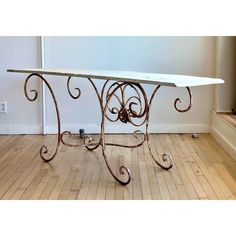 an iron and marble dining table in the middle of a wood floored room with white walls