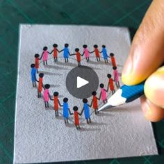 someone is holding a pencil and drawing a group of people on a piece of paper