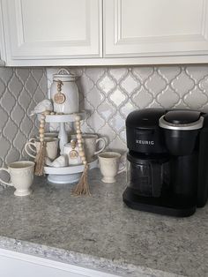 a coffee maker sitting on top of a kitchen counter next to mugs and saucers