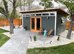 a small gray shed with an orange door sits in the middle of a yard next to a tree