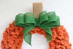 an orange and green knitted wreath hanging on a white wall with a burlock bow