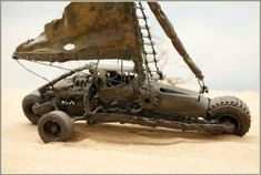 a toy car made out of metal on the sand with a sailboat in the background