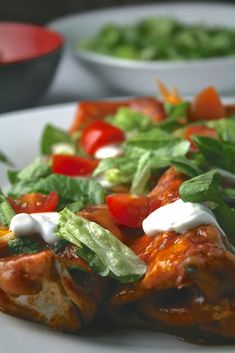 a white plate topped with meat covered in sauce and veggies next to salad