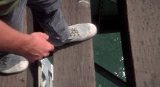 a man is standing on a dock with his feet in the water while holding onto another person's shoes