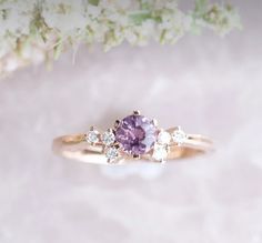 a close up of a ring with a purple stone and three white diamonds on it