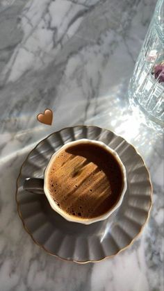 a cup of coffee on a saucer next to a vase with flowers in it