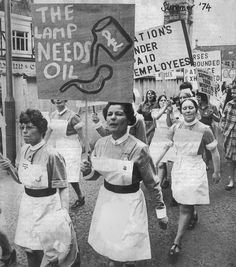 black and white photograph of women marching down the street in aprons holding up signs