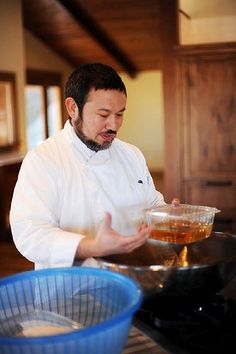 a man is cooking in the kitchen while wearing a chef's coat and holding a bowl