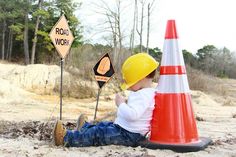 a little boy sitting on the ground next to a road work sign and traffic cone