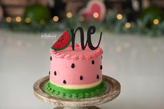 a pink cake with watermelon on top and the word one written in cursive writing