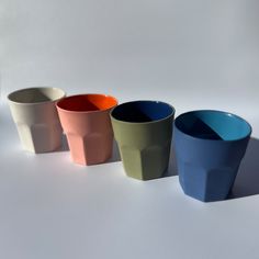 four different colored cups are lined up in a row on a white surface, with one empty cup to the side