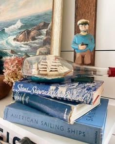 a stack of books sitting on top of a table next to a vase with a ship in it