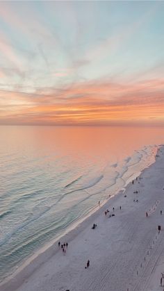 an aerial view of people walking on the beach at sunset or sunrise with pink and blue colors