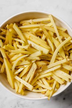 a white bowl filled with sliced potatoes on top of a marble countertop next to a knife