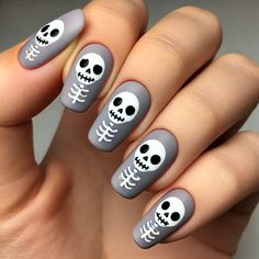 Bring some playful spookiness to your Halloween look with this adorable skeleton-themed nail design! These rounded, matte gray nails feature cute and simple white skeletons with smiling skull faces, adding a fun and quirky twist to the spooky season. Perfect for those who love a Halloween manicure that’s more charming than scary, this design is sure to delight and bring a smile to anyone who sees it. Embrace the Halloween fun with these cute skeleton nails! #HalloweenNails #SkeletonNails #CuteNailArt #SpookySeason #NailDesign #HalloweenManicure #FunNails Nails Skull Designs, Skeleton Nails Acrylic, Nail Art Skull, Gray Halloween Nails, Skeleton Nails Designs, Skeleton Halloween Nails, Halloween Skull Nails, Halloween Nails Skeleton, Halloween Nail Ideas Simple