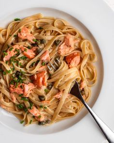 pasta with salmon and capers on a white plate next to a silver serving spoon