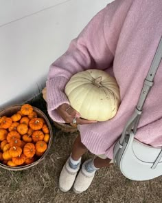 a woman holding a pumpkin next to a bowl of baby carrots