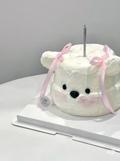 a white cake with a pink ribbon around it and a teddy bear on the top