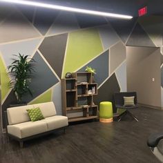 a room with a couch, chair and bookshelf in front of a colorful wall