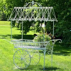 a small white cart with flowers in it on the grass next to some trees and bushes