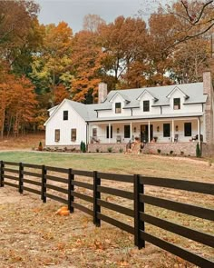 a large white house sitting in the middle of a field next to a wooden fence