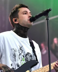 a man with tattoos on his face and neck playing a guitar in front of a microphone